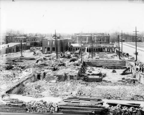 View of demolition near Civic Center, 14th and Broadway, in Denver, Colorado. Brick and lumber is strewn around remaining foundations; houses and apartment buildings are in the background. (1916-1918)