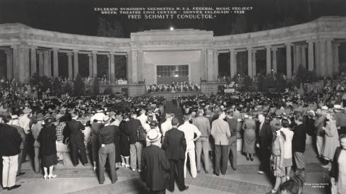 Night view of a Colorado Symphony Orchestra concert at the Greek Theater and Colonnade of Civic Benefactors in Civic Center Park, Denver, Colorado (designed by Marean and Norton). Well dressed people crowd the plaza; signs read: "Concert 8 P.M. Tonight," "USA Work Program WPA," "On The Air With KLZ," and "Town Talk Milk Bread." (1938)