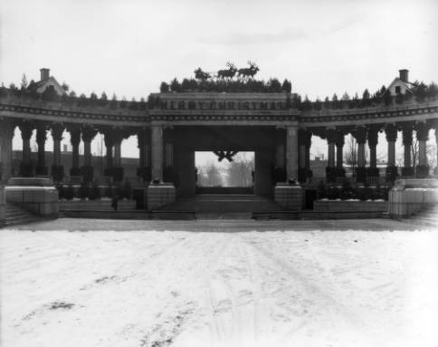 View of the central portion of the open air Greek Theater and Colonnade of Civic Benefactors with Christmas decorations, Civic Center Park, Denver, Colorado. Santa with his reindeer are above the stage area. "Merry Christmas" letters are along the frieze and a wreath hangs down into stage opening. (1920-1925)