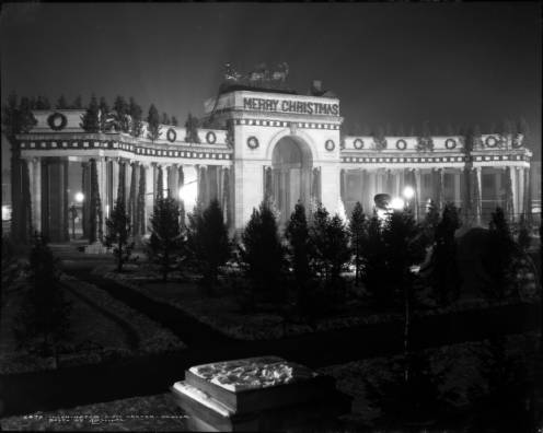 View of Voorhies Memorial with Christmas decorations, Civic Center, Denver, Colorado, shows wreaths and garlands on gateway and colonnade, "Merry Christmas" sign, Christmas trees, and Santa Claus with reindeer atop gateway. (1927)