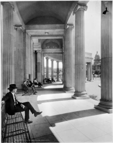 Interior view of the Voorhies Memorial pergola, west toward the capitol, in Denver Colorado's Civic Center (Fisher and Fisher, architects); Denver artist, Allen True painted silhouette buffaloes directly on concrete, high on lunette of arch; people sit on wire benches under roof of colonnade. (1922-1925)