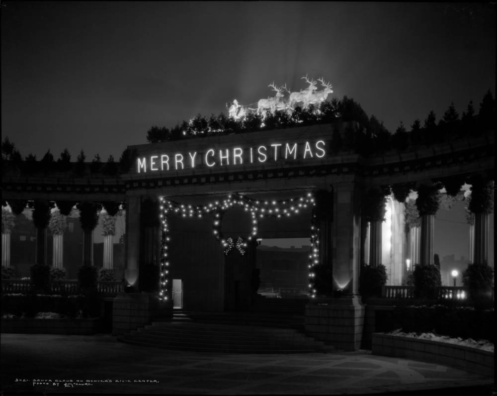 Night view of Greek Theater and Colonnade of Civic Benefactors, West Fourteenth (14th) and Acoma Street, Civic Center, Denver, Colorado; Christmas decorations on the Colonnade include: spotlit Santa Claus and his reindeer top arch; "Merry Christmas" illuminated across frieze, evergreen garland wrapped columns, large wreath with bow centered bordered by evergreen garland strung out to sides of archway, laced with lights; snow on sides of theater steps; streetlights and interior of colonnade illuminated. (1929)