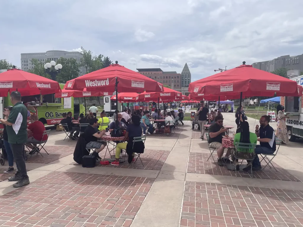Photo of people enjoying food under red umbrellas at Civic Center EATS