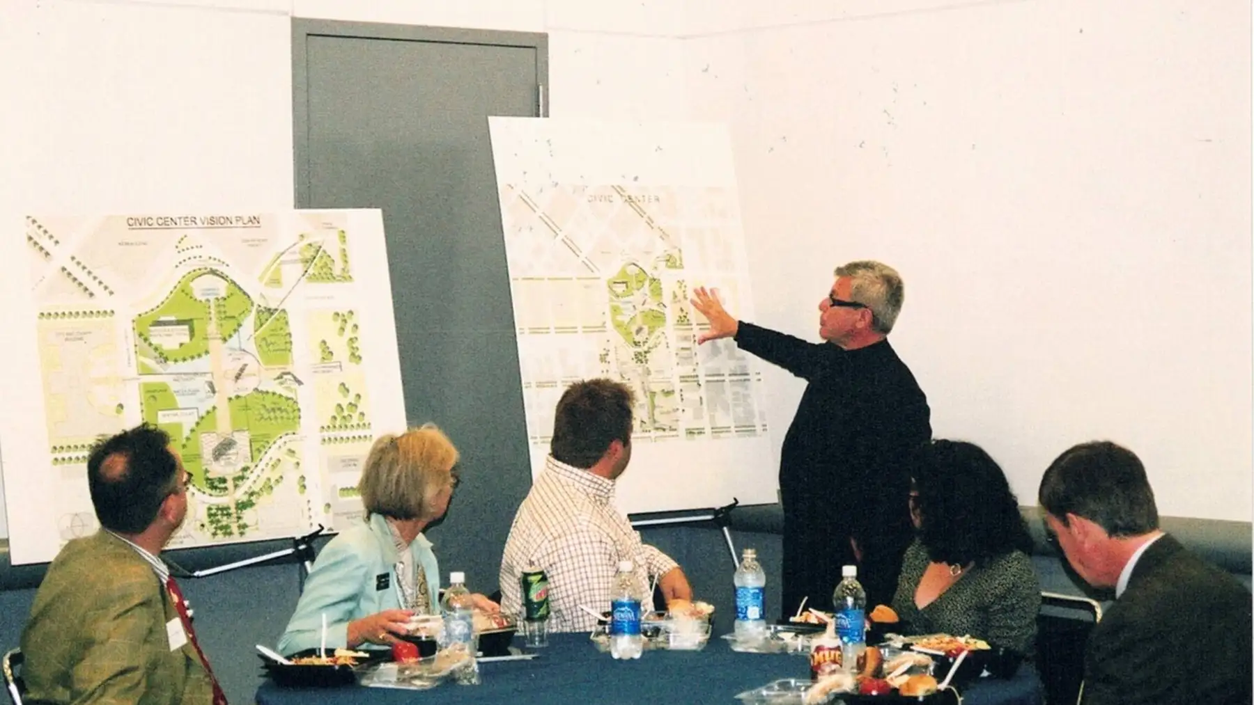 A team sits in a room looking at large posters of the "Civic Center Vision Plan"